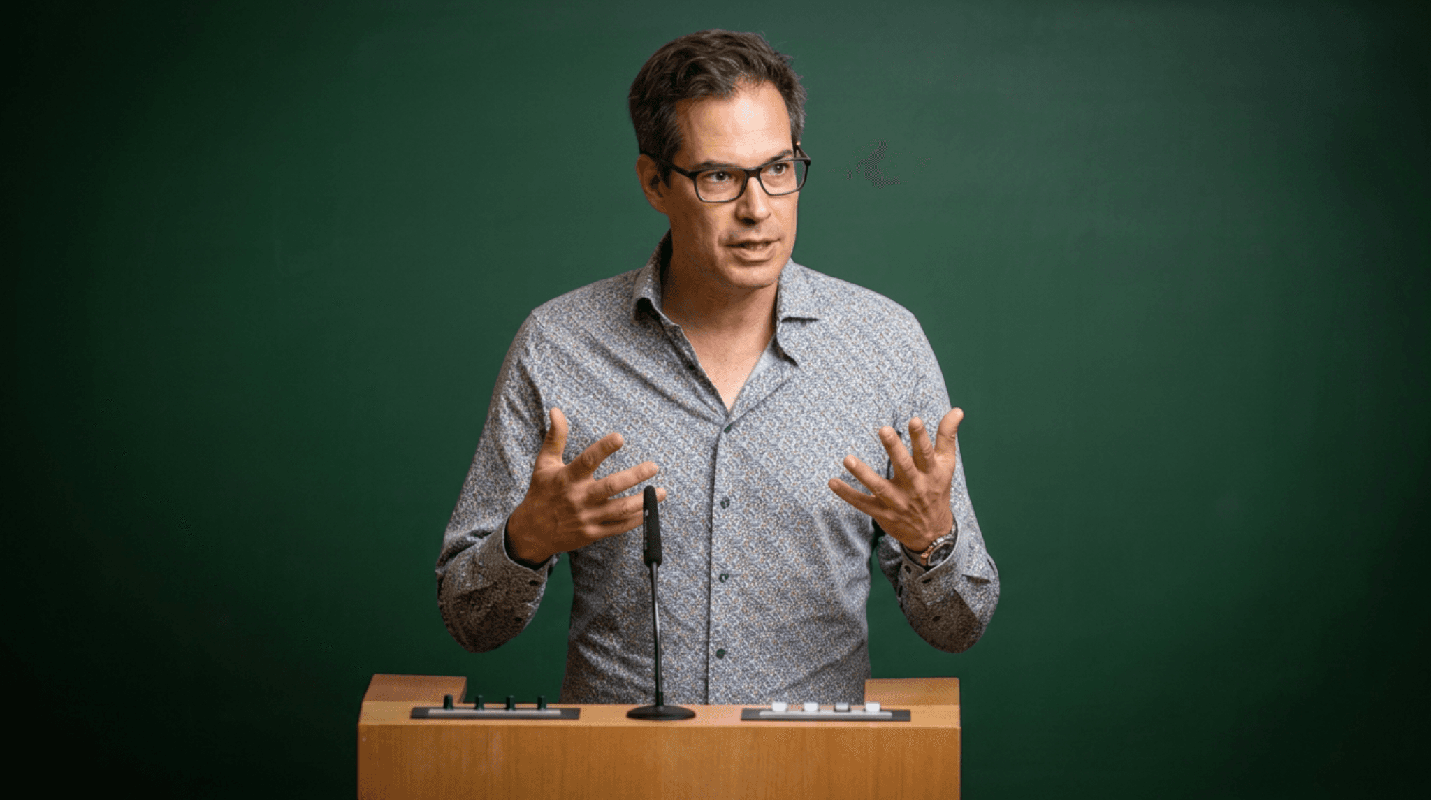 Prof. Dr. Markus Huff speaks and gestures at a lectern against a green background.